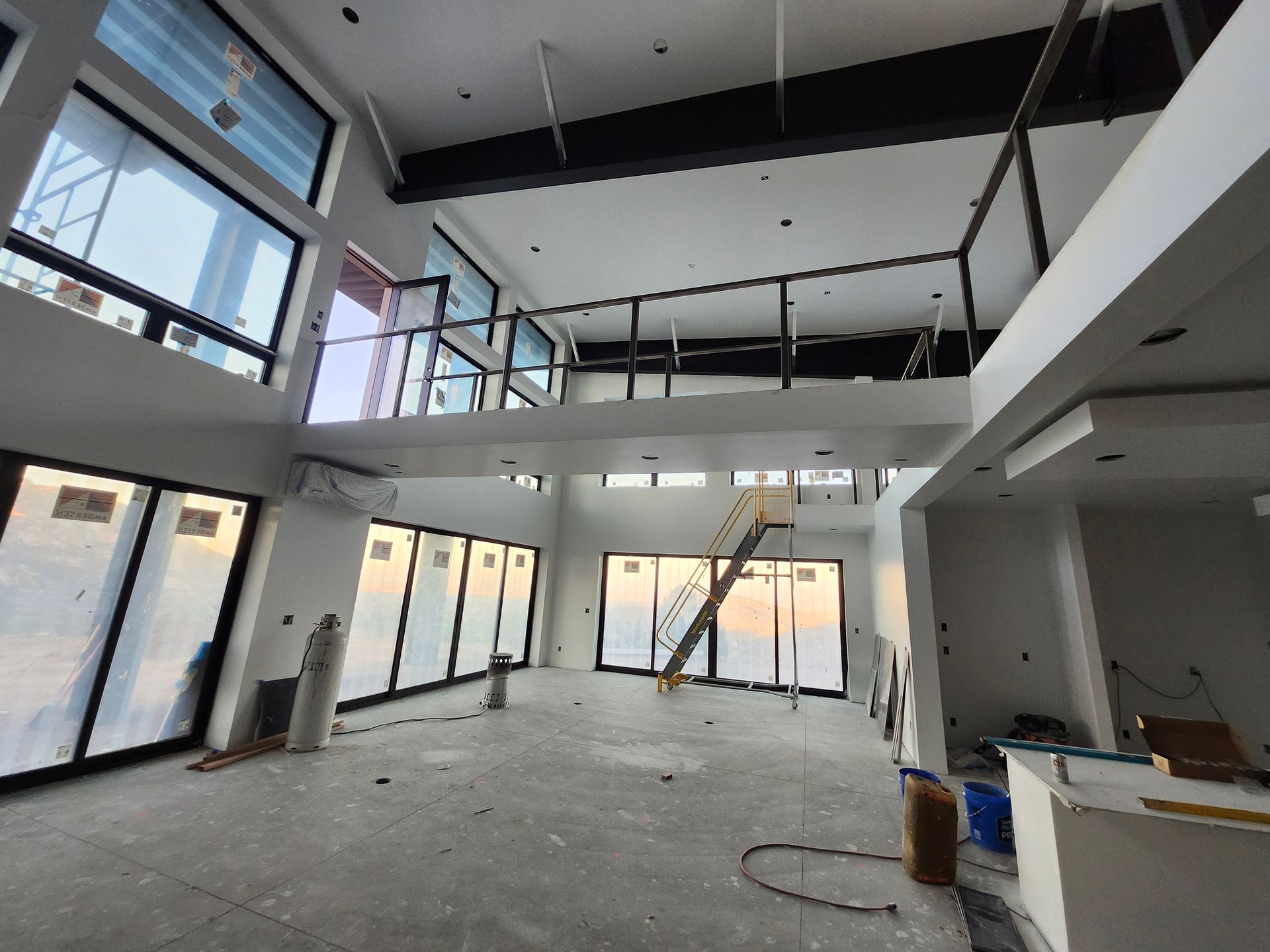 Interior of a modern home under construction; large windows, glass railing, high ceilings, unfinished walls.