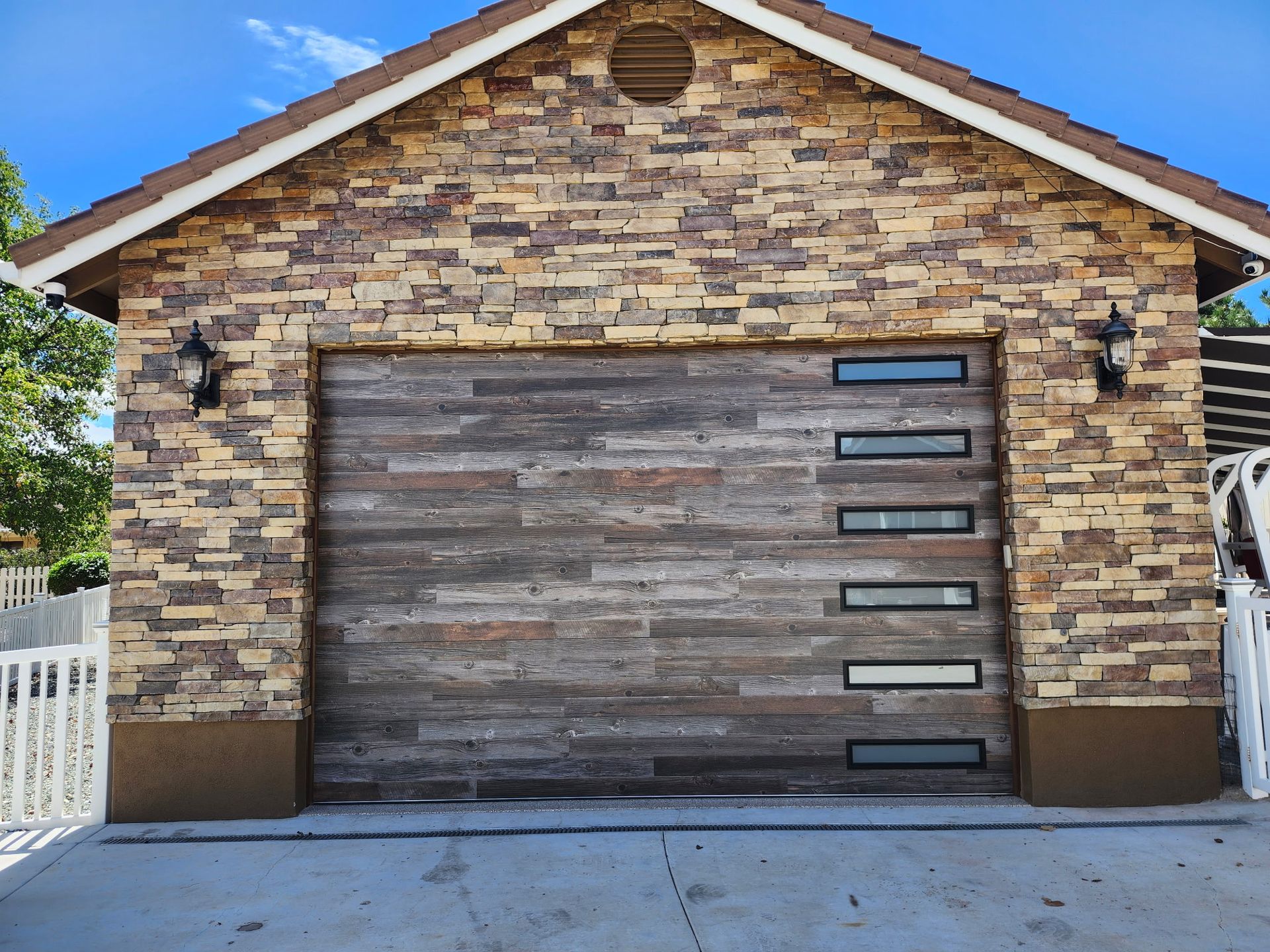 Garage with stone facade and a weathered wood garage door with glass panels.
