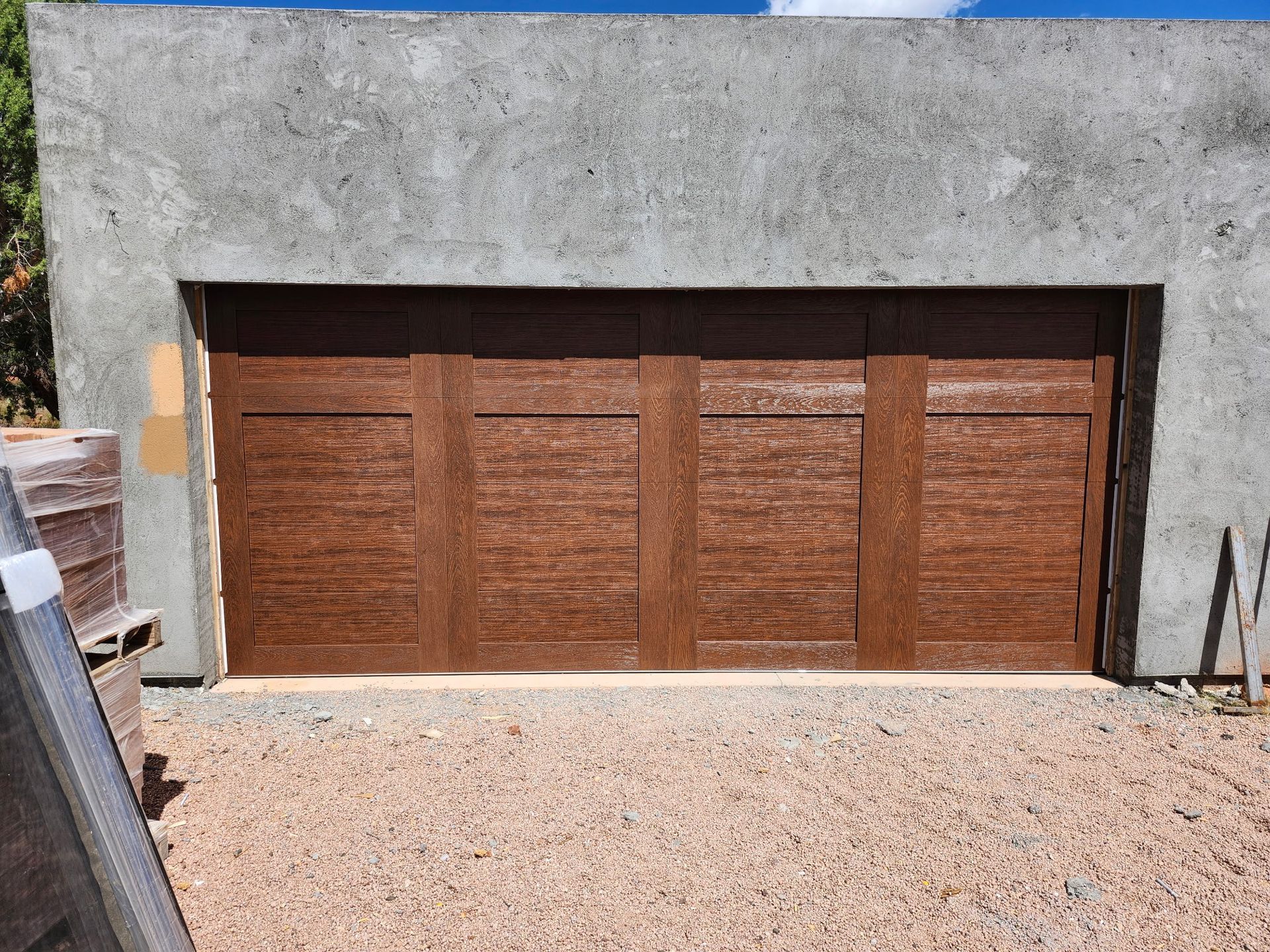 Brown garage doors set in a concrete structure, gravel driveway.