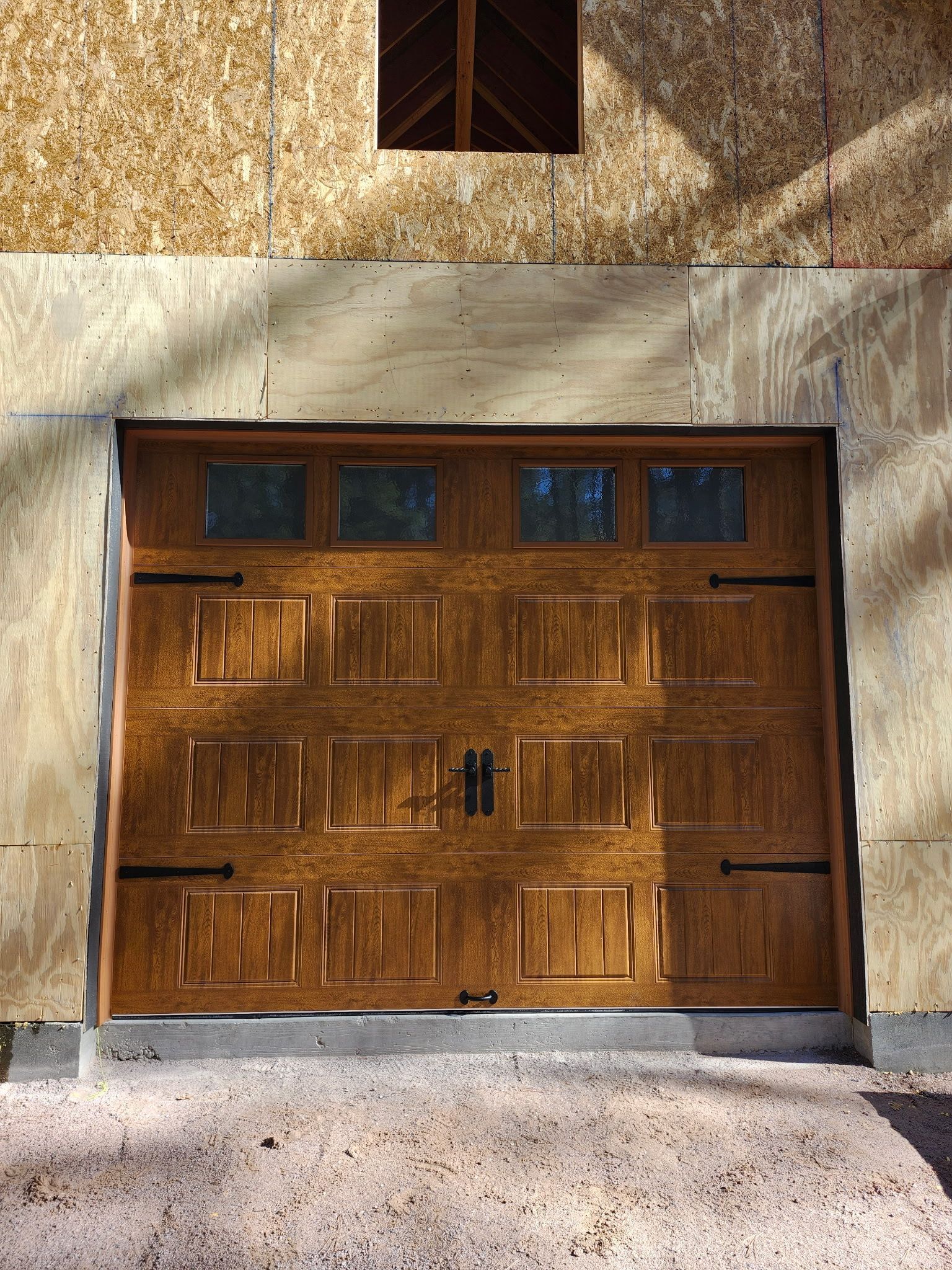 Wooden garage door with windows, black hardware. Building exterior with a small, dark window above.