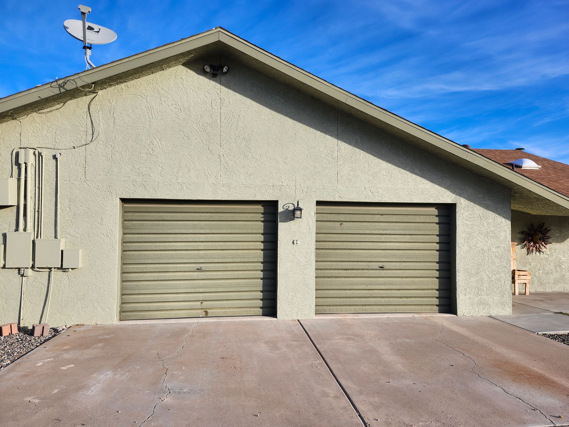 Two-car garage with tan stucco exterior and green doors; a satellite dish is mounted on the roof.
