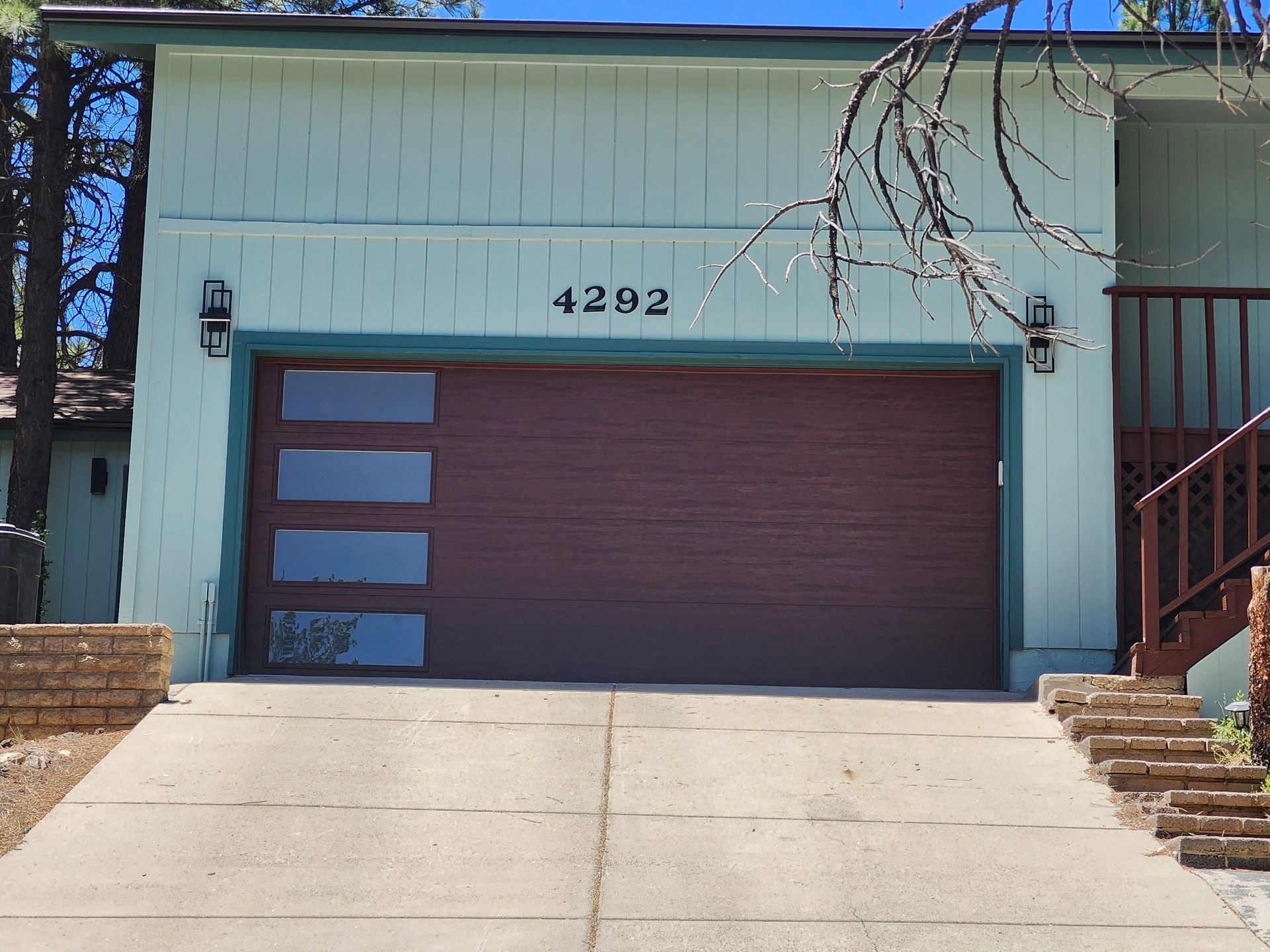Brown garage door with frosted windows, teal house with address 4202 on it.