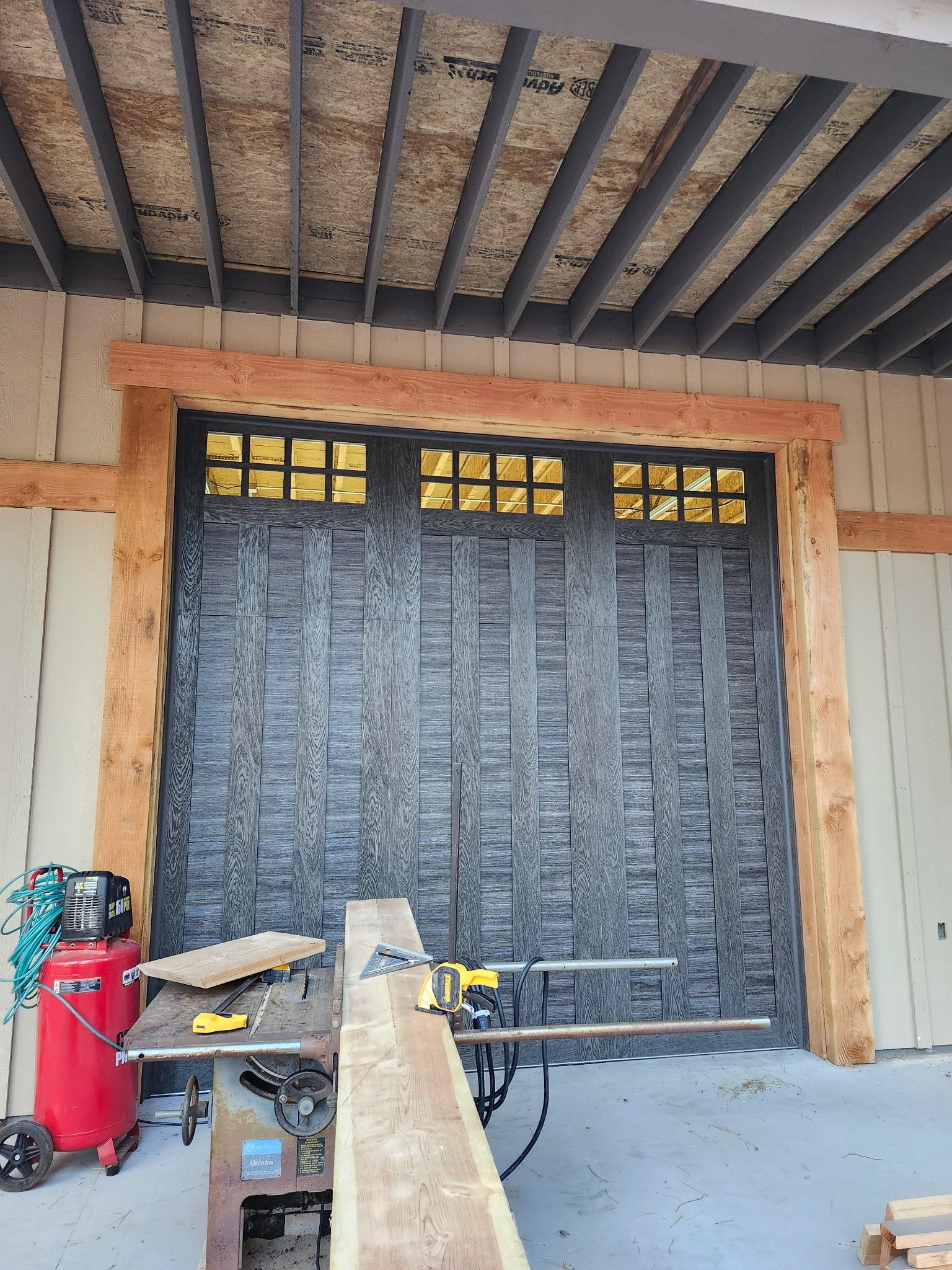 Black garage door with textured pattern, yellow window panes, surrounded by light wood framing.