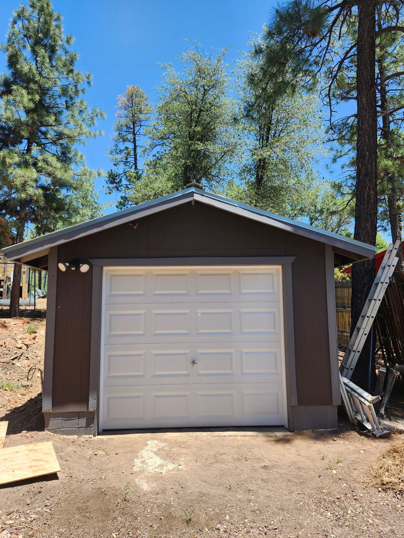 Brown and white garage with a metal roof, set against a backdrop of trees and a bright blue sky.