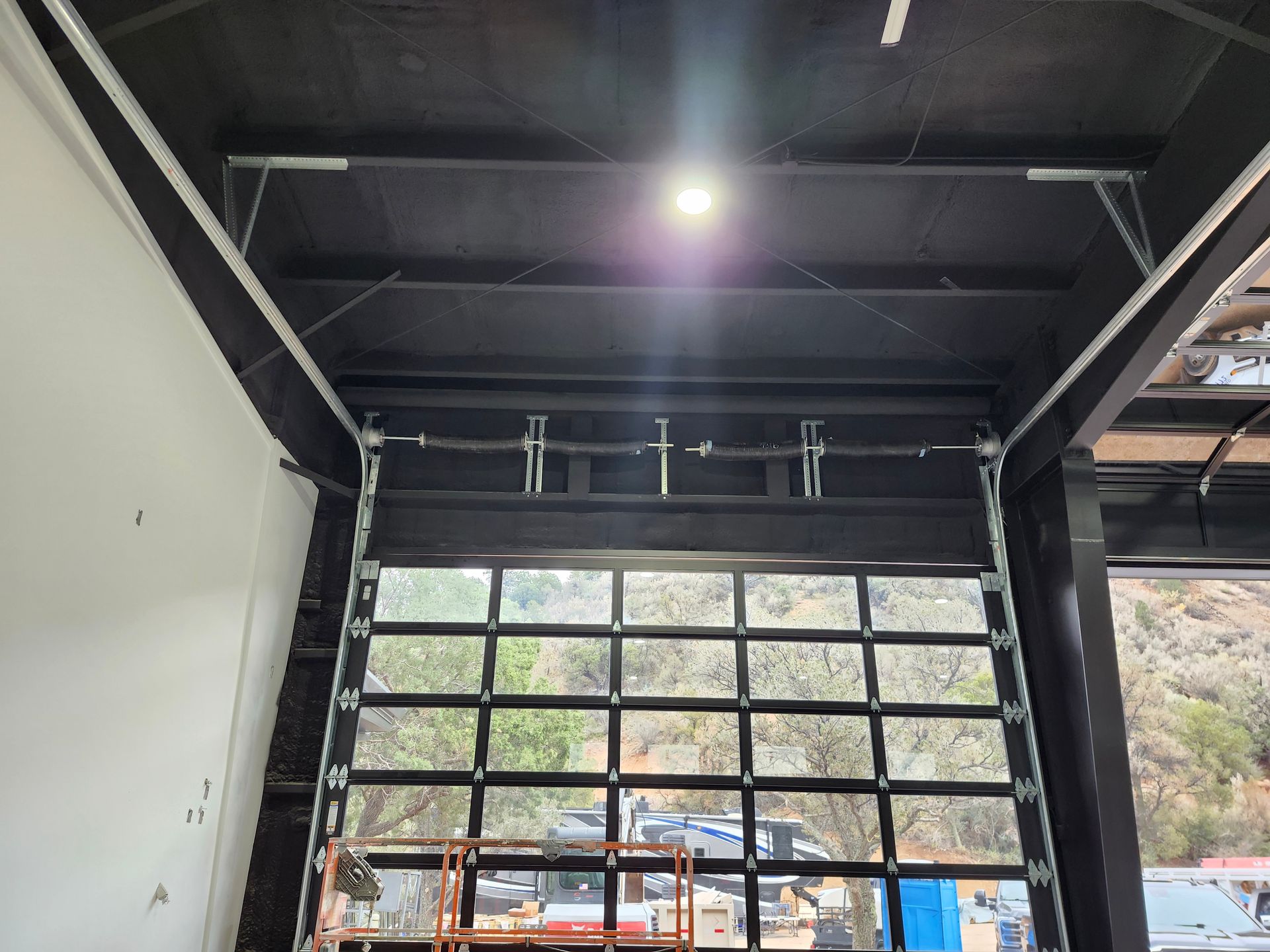 Interior view of a garage door with a clear glass window, black frame, and bright overhead lighting.