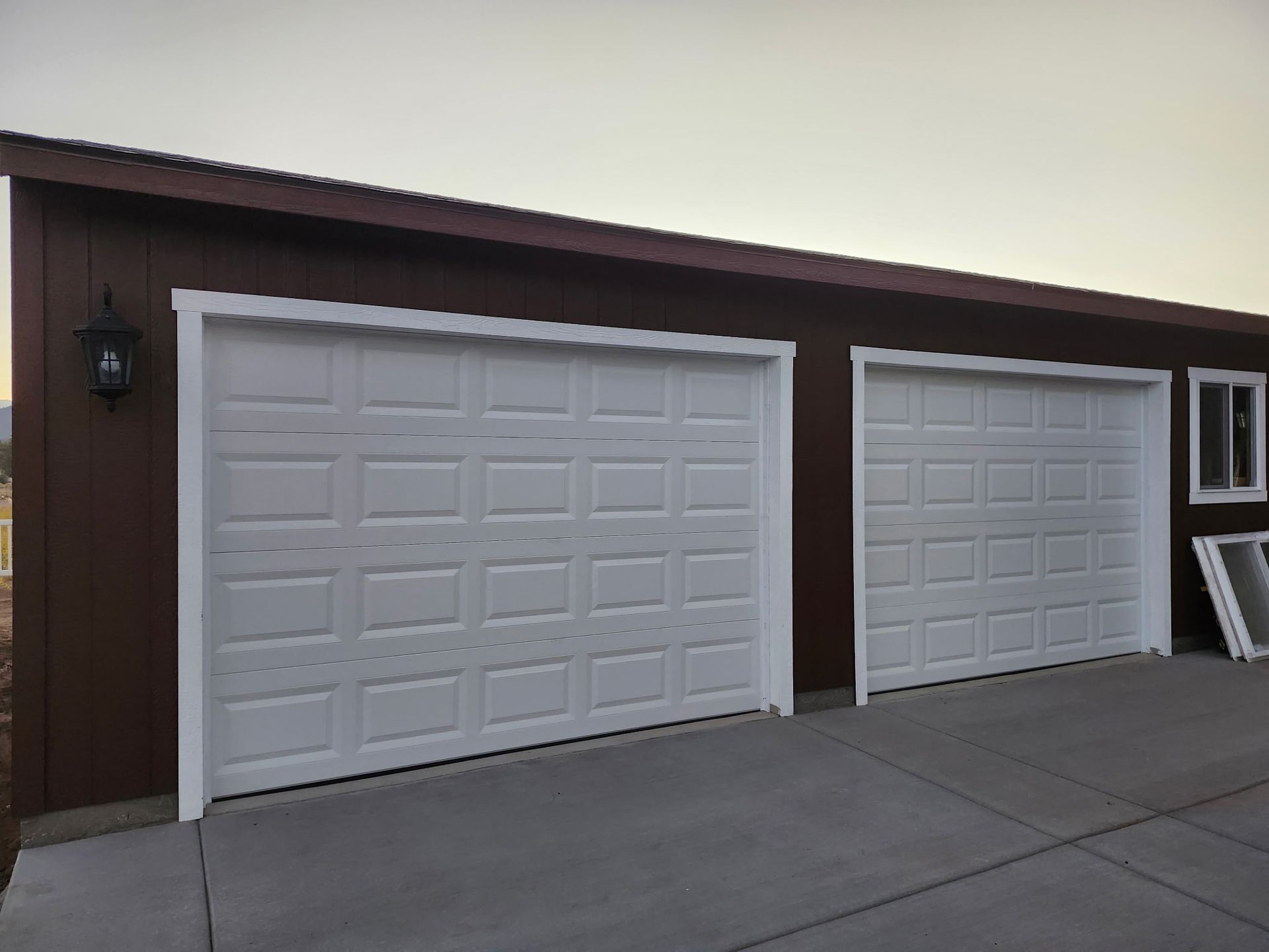 Brown garage with two white panel doors and a small window. Concrete driveway.