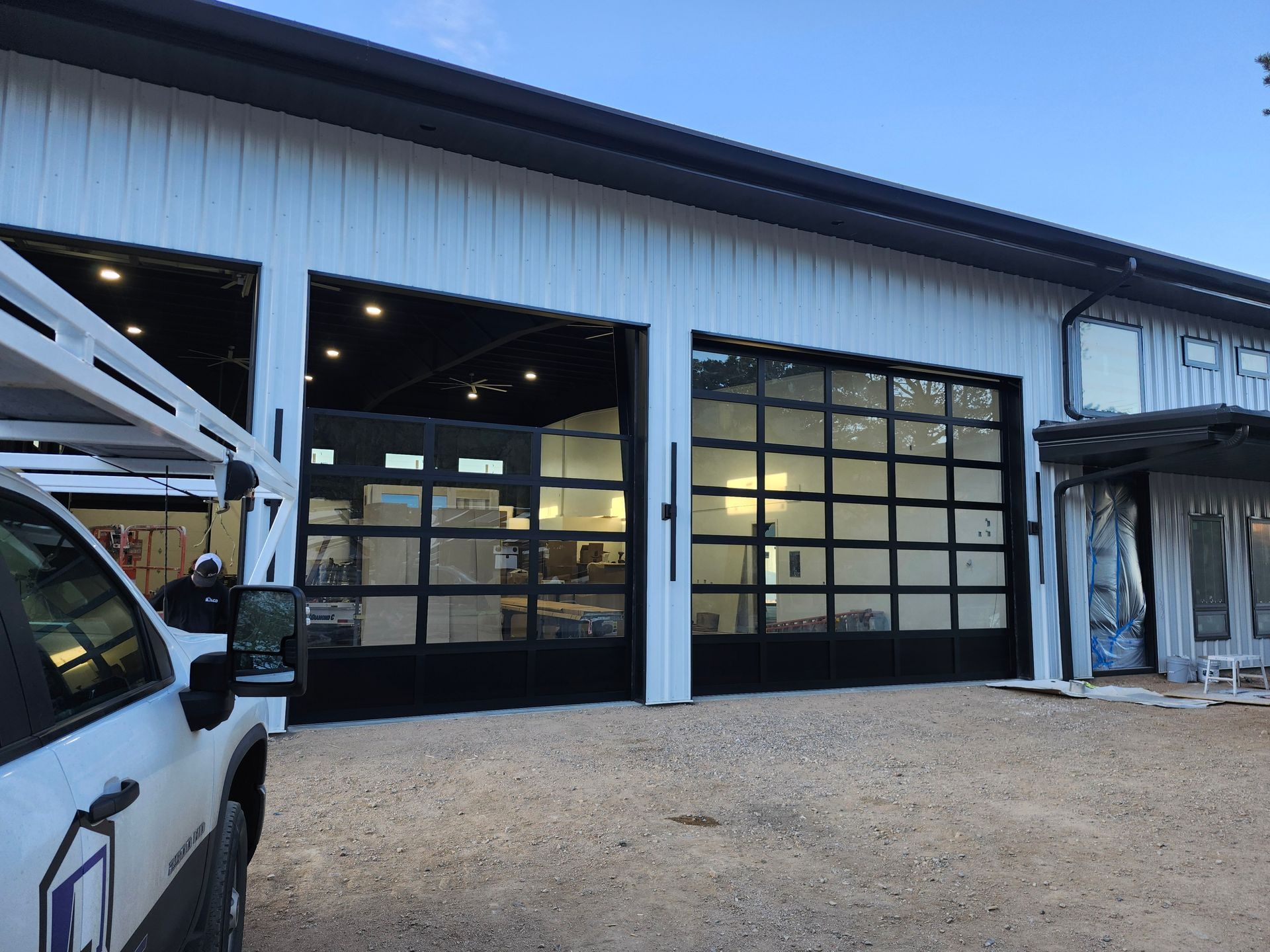 Exterior of a white building with black framed glass garage doors open. A white work truck is parked to the left.