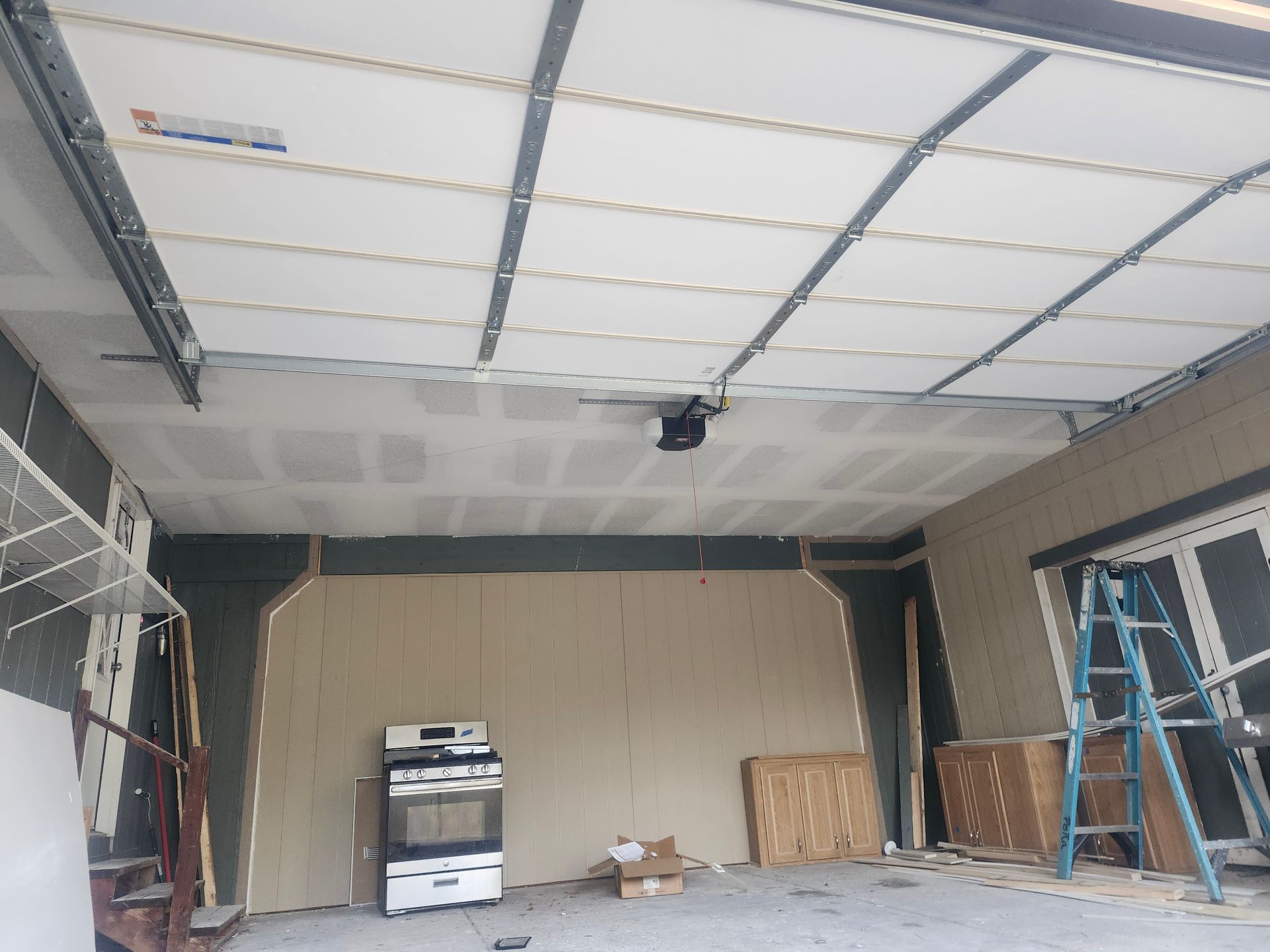 Garage under construction, showing a partially installed garage door, drywall, and a stove.