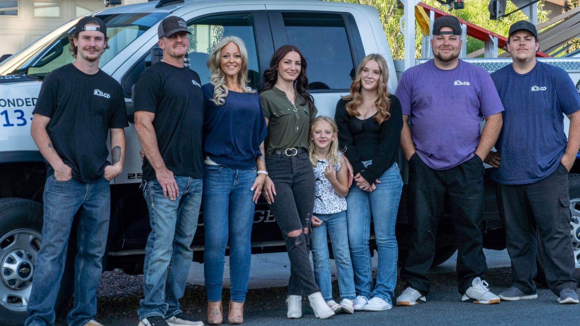 Group of people standing in front of a white truck; smiles and casual attire.