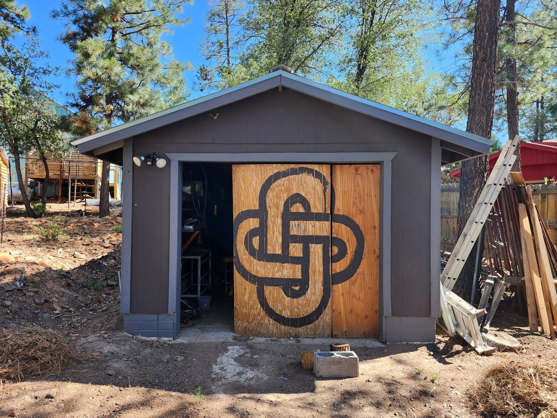 Garage with wood doors featuring a black knot design. Gray exterior, open doorway, trees in the background.