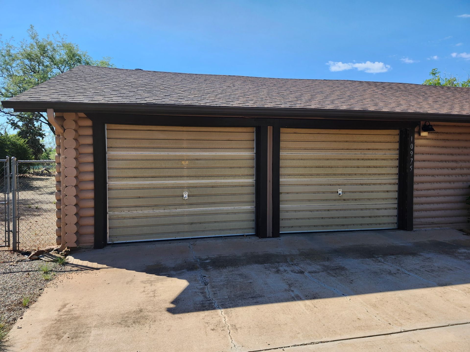 Two-car garage with tan doors and a brown roof against a blue sky.