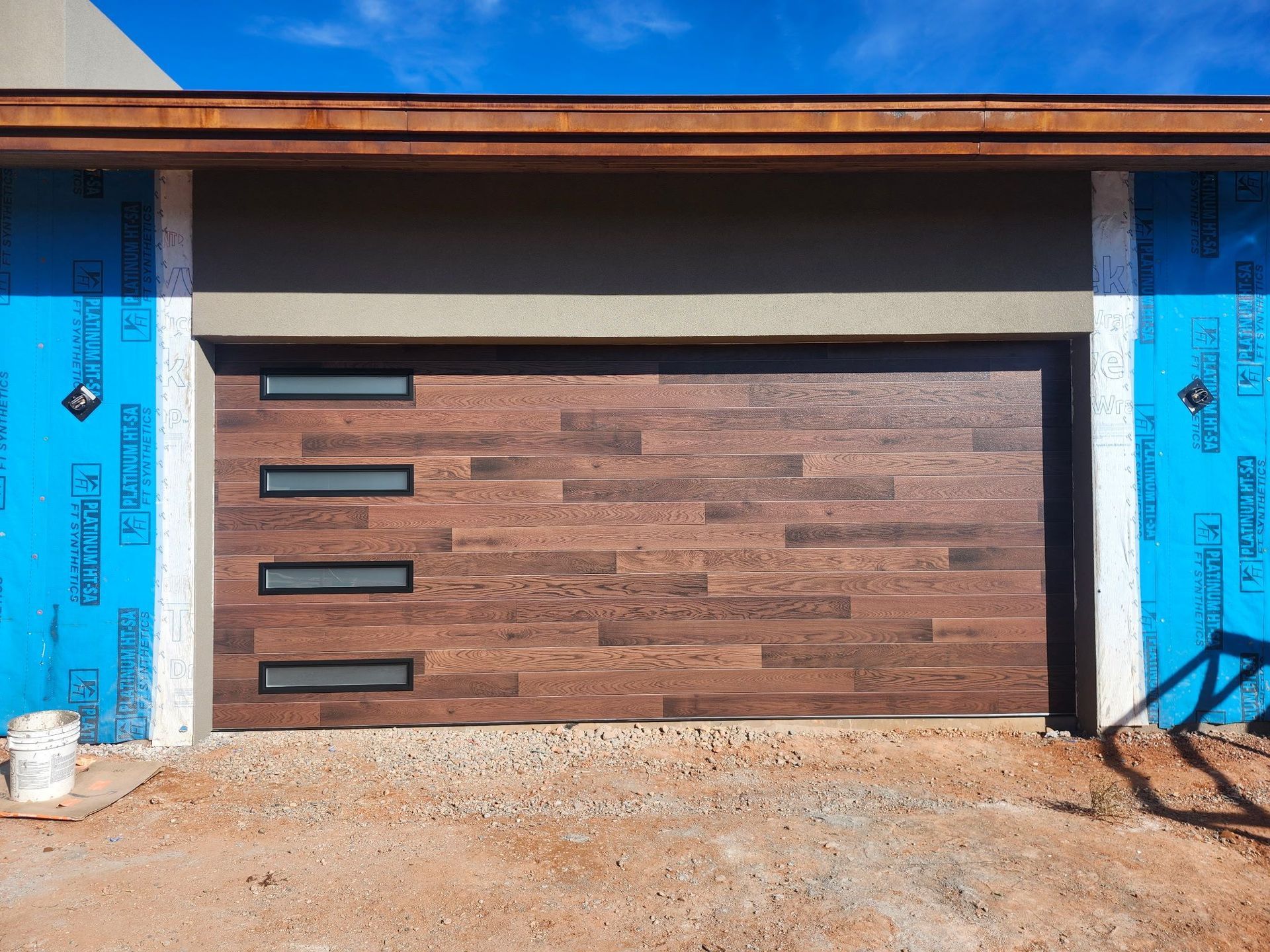 Brown, wood-look garage door with three horizontal window panels, under construction.
