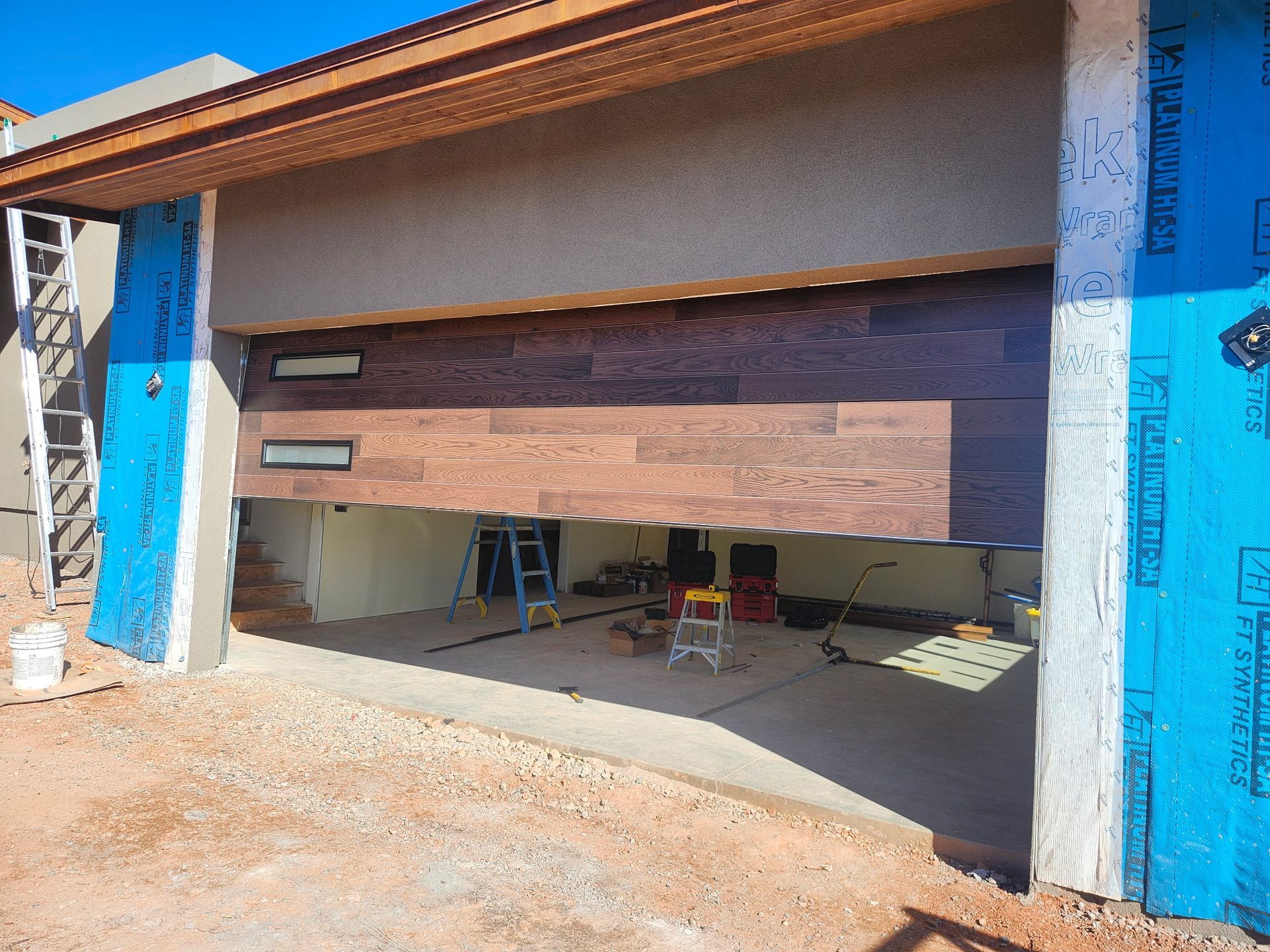 Garage door partially open during construction, brown facade, blue insulation, concrete driveway.