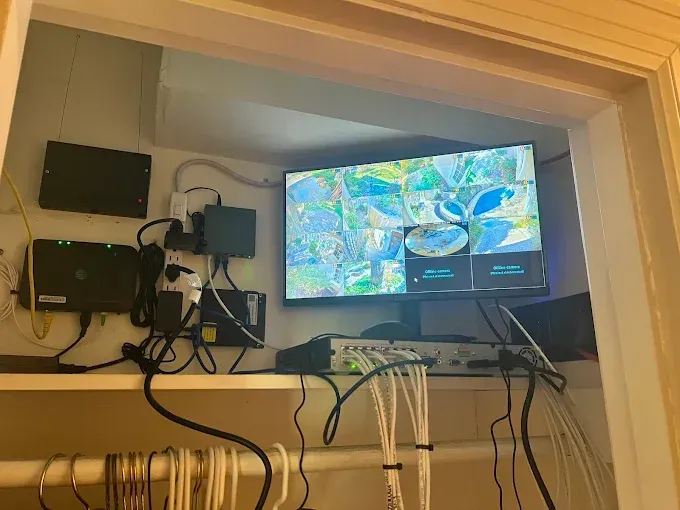 A security system setup inside a closet. Includes a TV displaying camera feeds, and various electronic components.