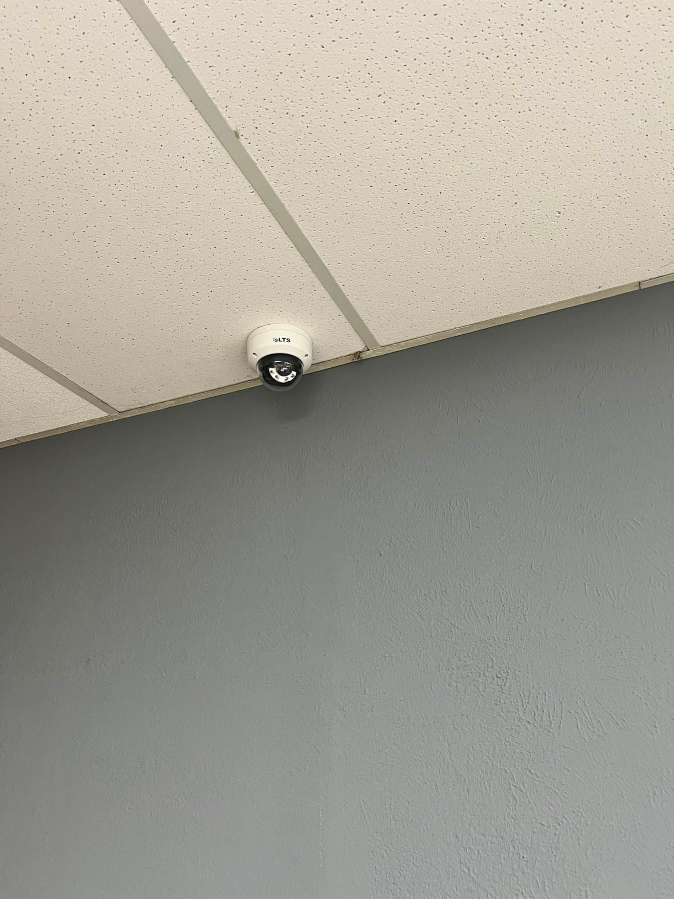 Security camera mounted on a white ceiling, above a gray wall.