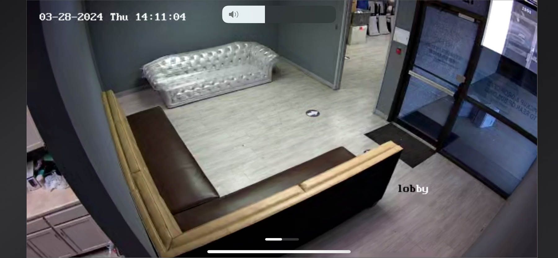 Lobby with gray flooring, a brown and tan sectional sofa, a tufted couch, and a glass door.