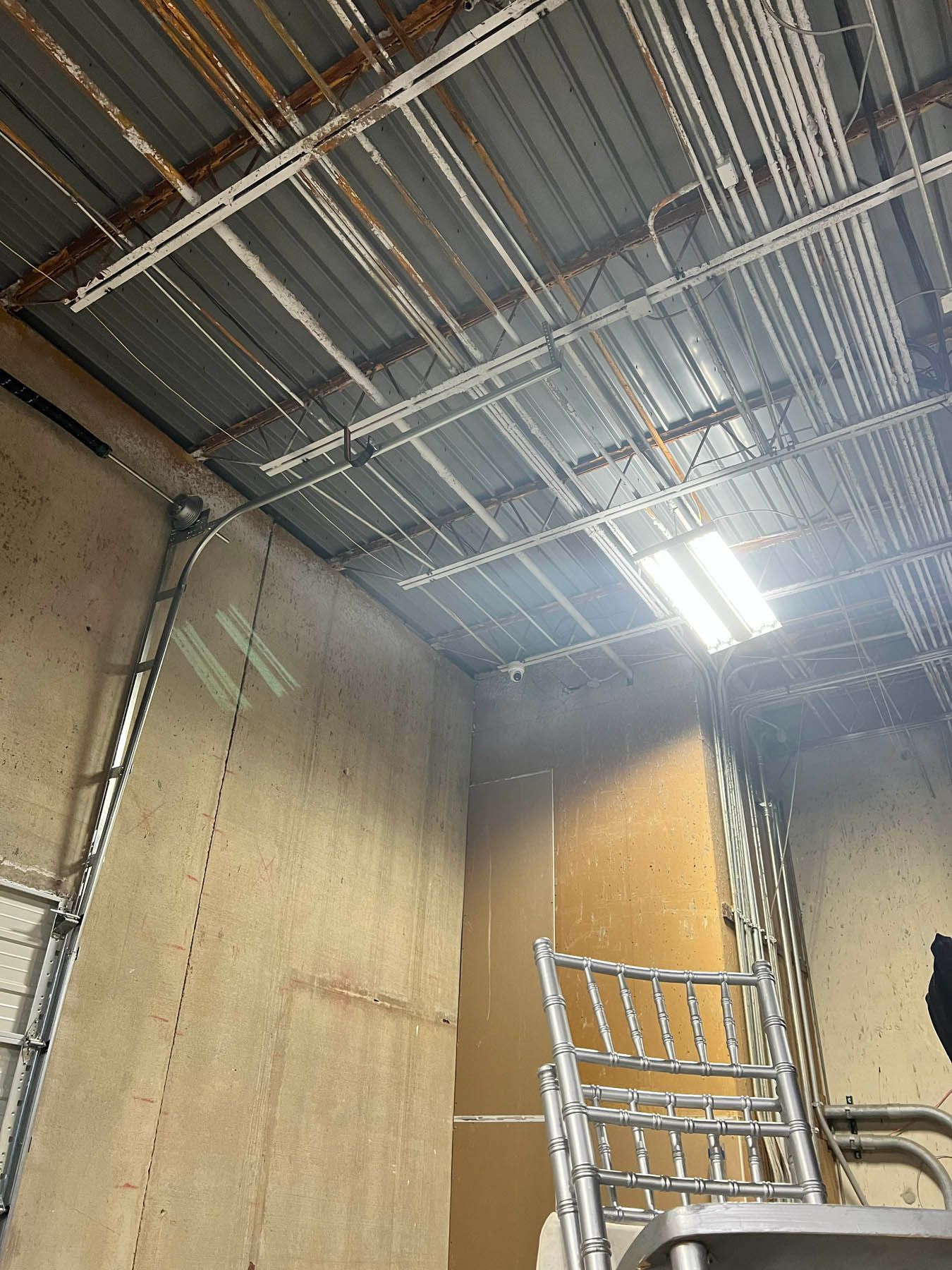 Ceiling with metal beams and wiring, concrete wall, and a chair.