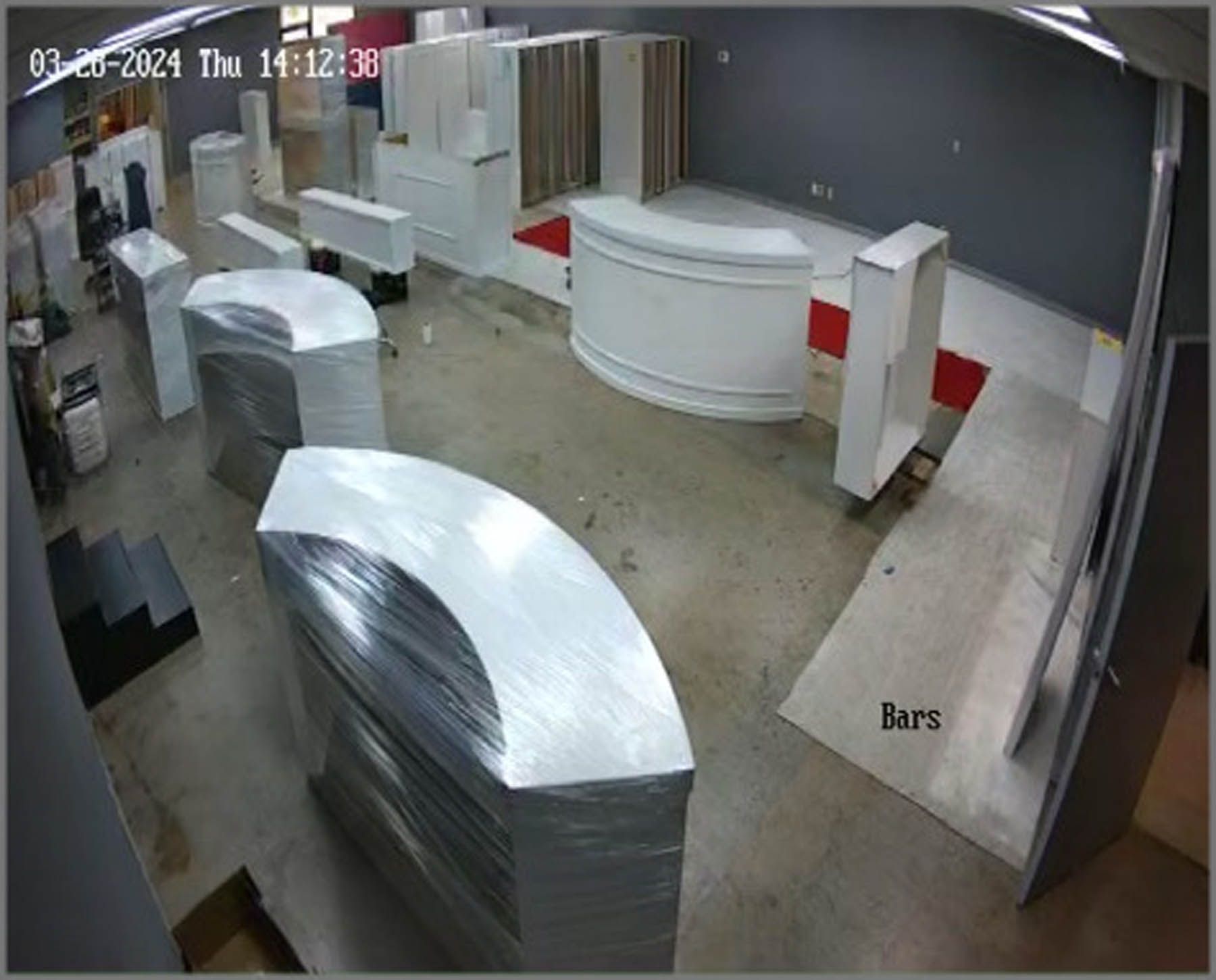 A high-angle view of a construction zone. White, curved structures wrapped in plastic dominate the space. Grey walls and floor.