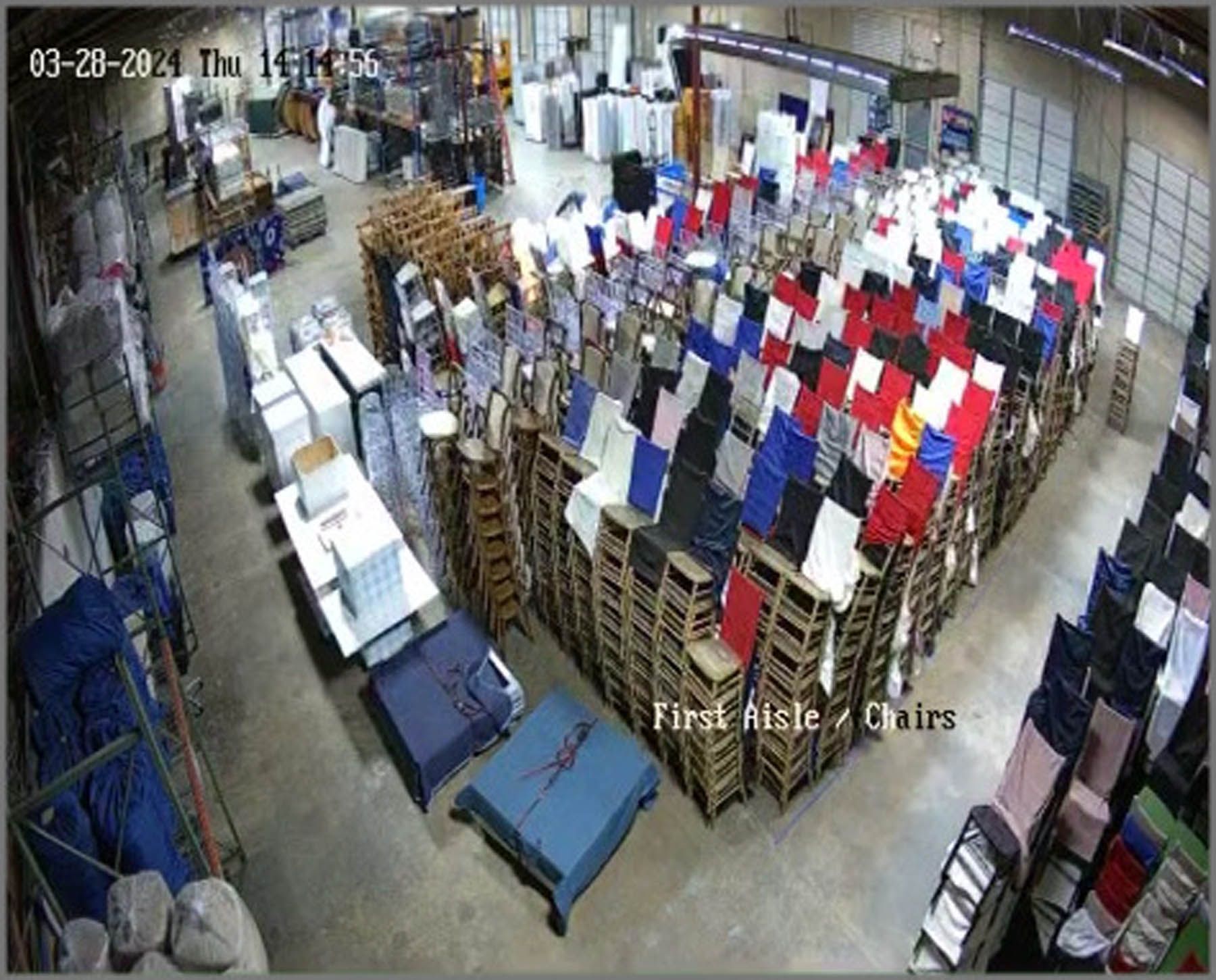 Warehouse with stacked pallets of textiles, mostly clothing. Overhead view, various colors.