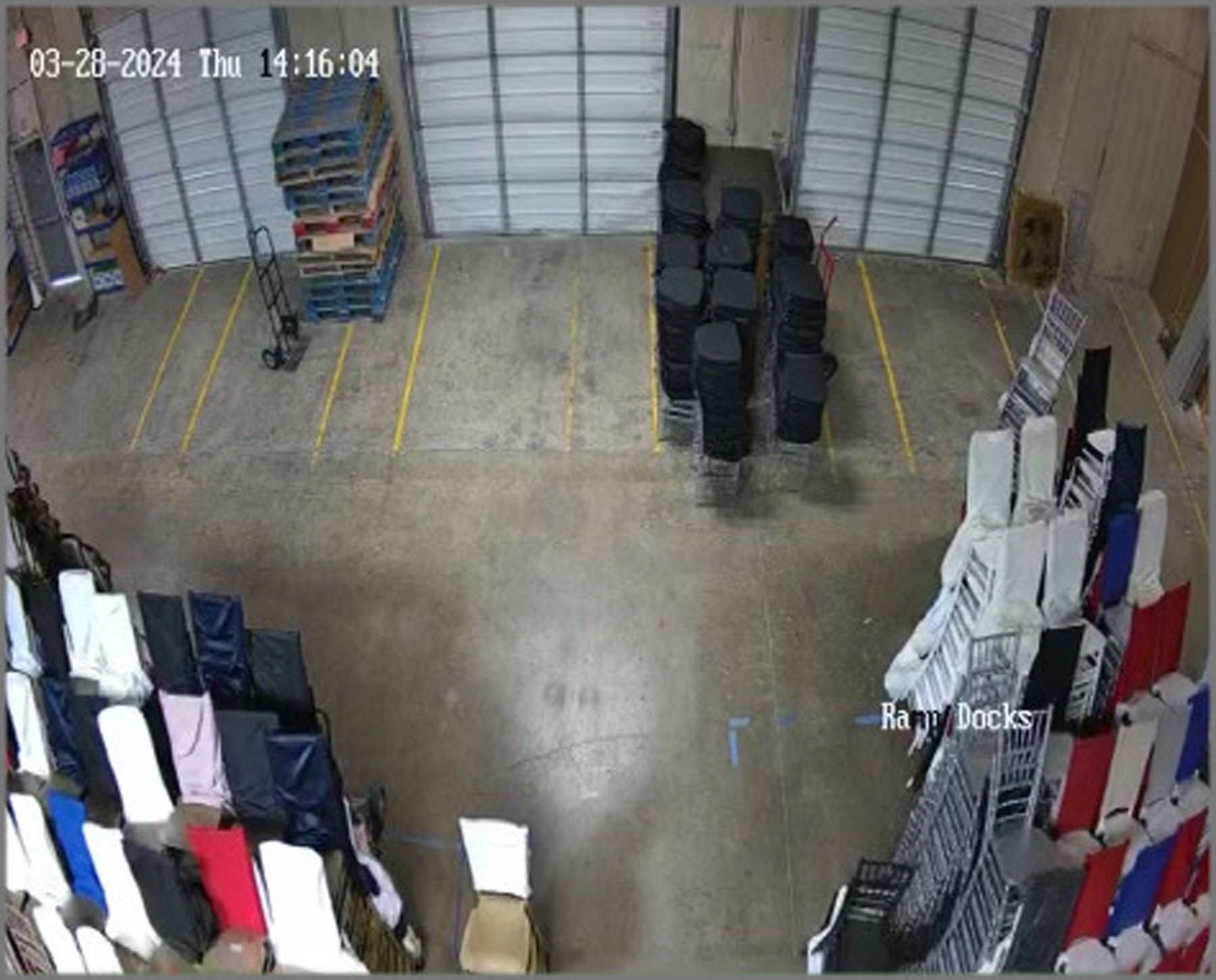 Warehouse interior with stacks of chairs, pallets, and a hand truck. Timestamp in top-left corner.