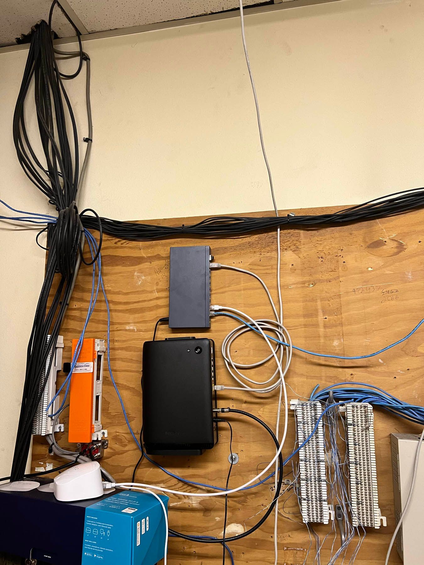 Network equipment mounted on a wooden wall, with tangled cables of various colors.