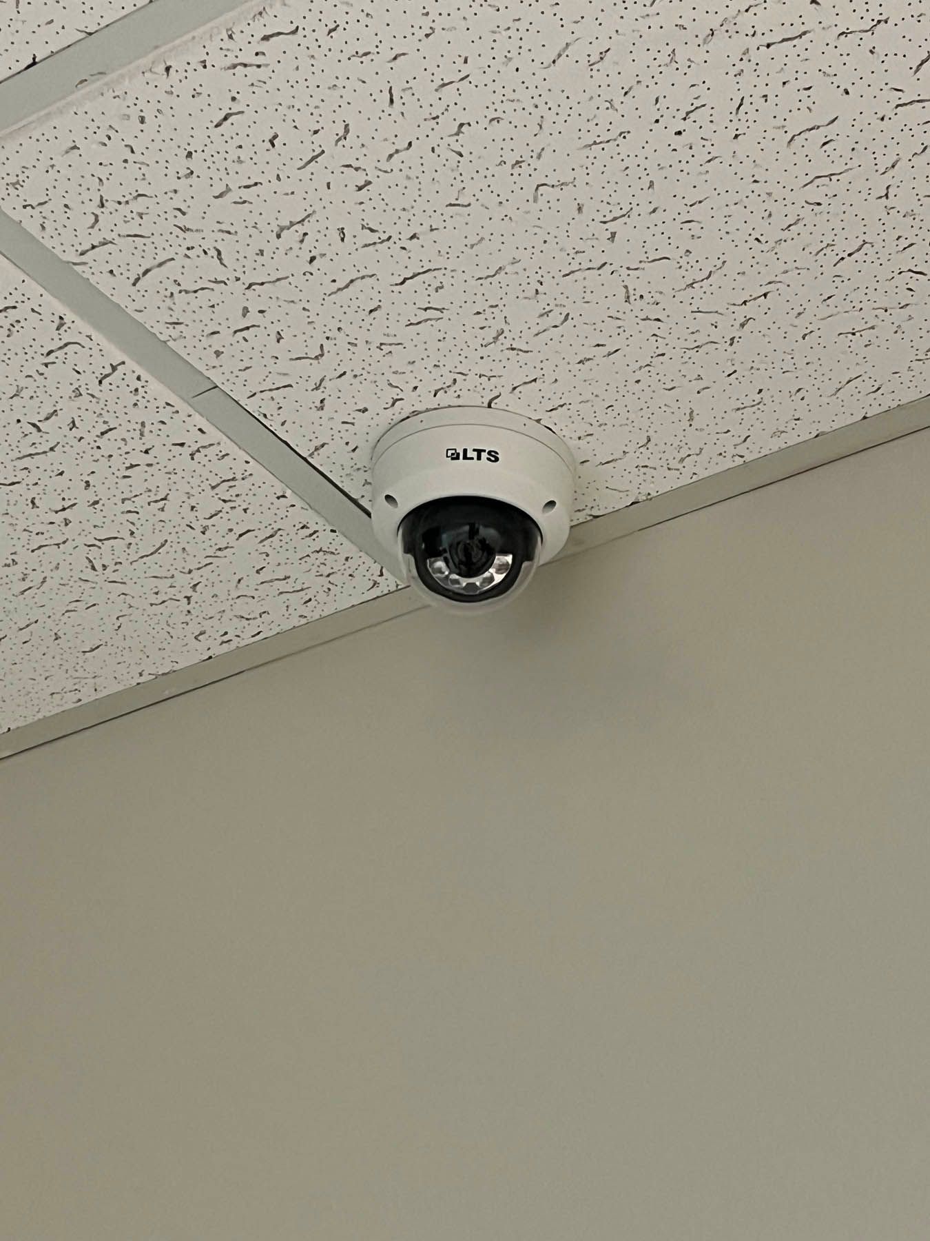 Security camera mounted on a white ceiling with a textured surface, above a beige wall.