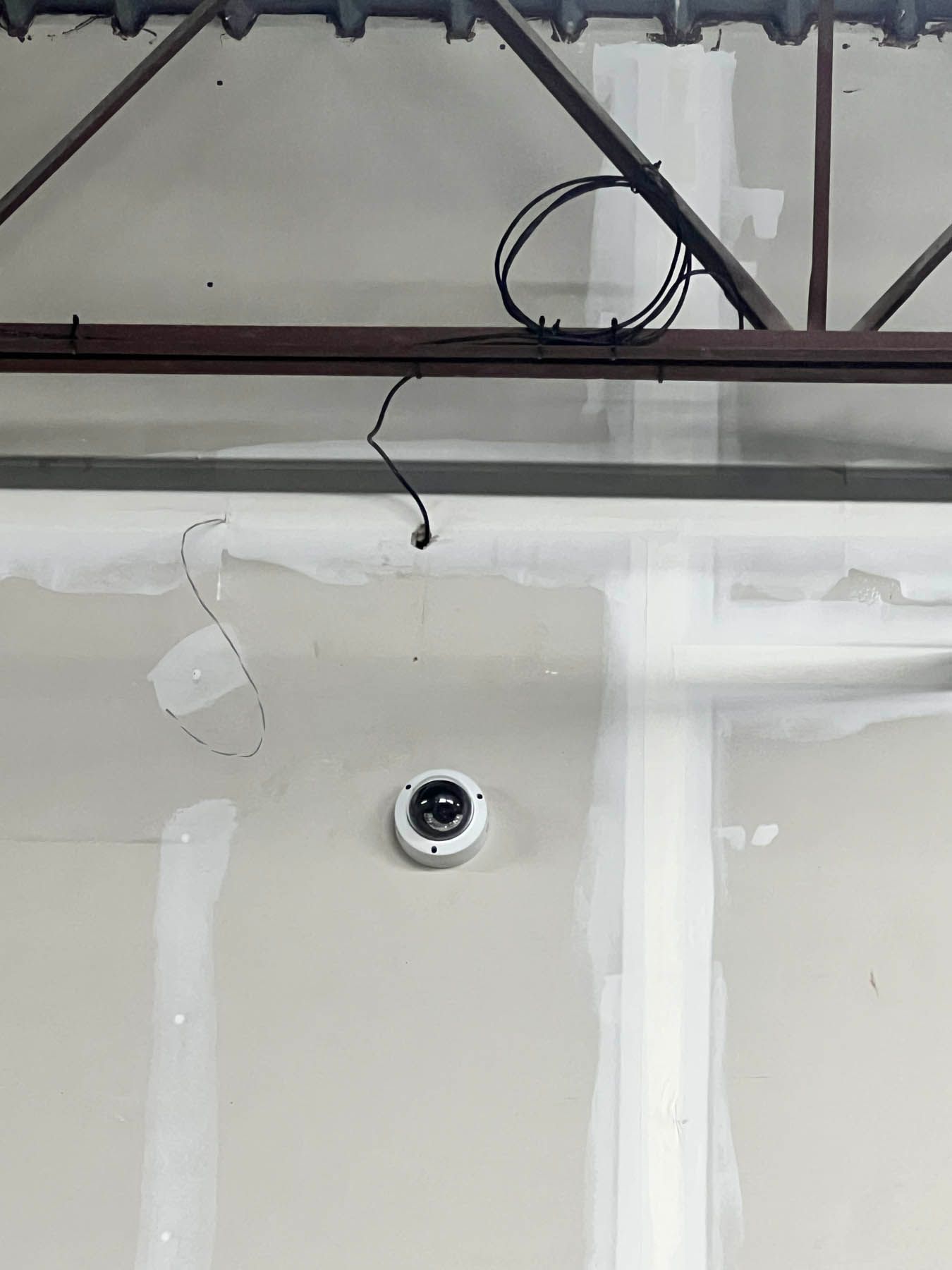 Security camera installed on a drywall wall under construction, with exposed beams and wiring visible.