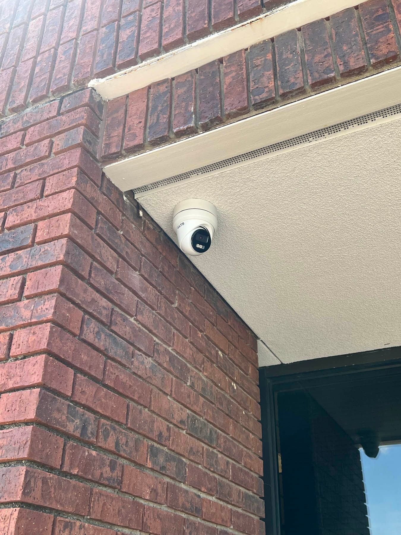 Security camera mounted on a building's brick wall, beneath a white overhang.