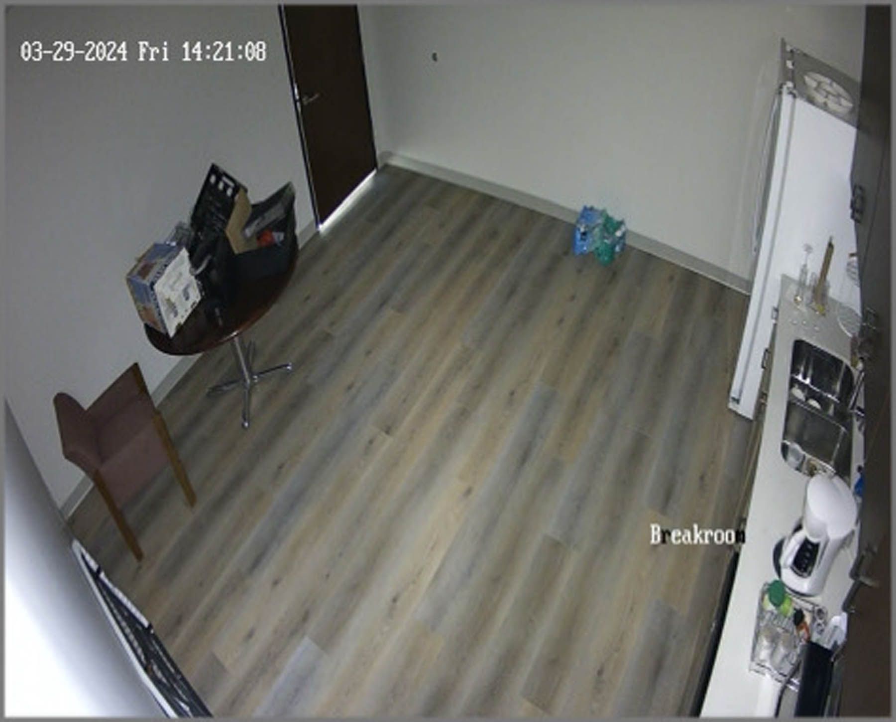 A breakroom with a table, chair, and a counter. There's also water bottles on the floor and a closed door.