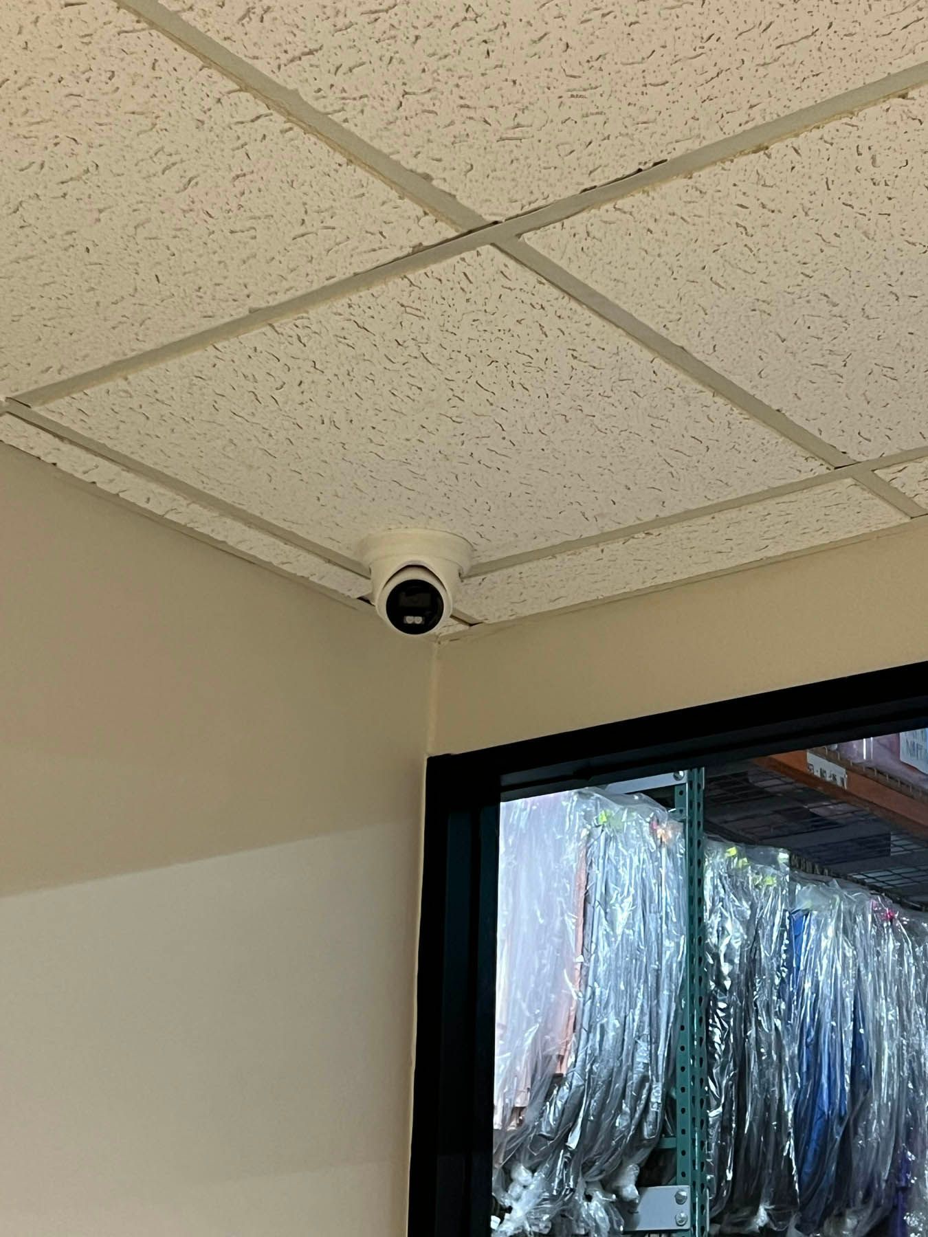 Security camera mounted on a drop ceiling, corner of a room with a window.