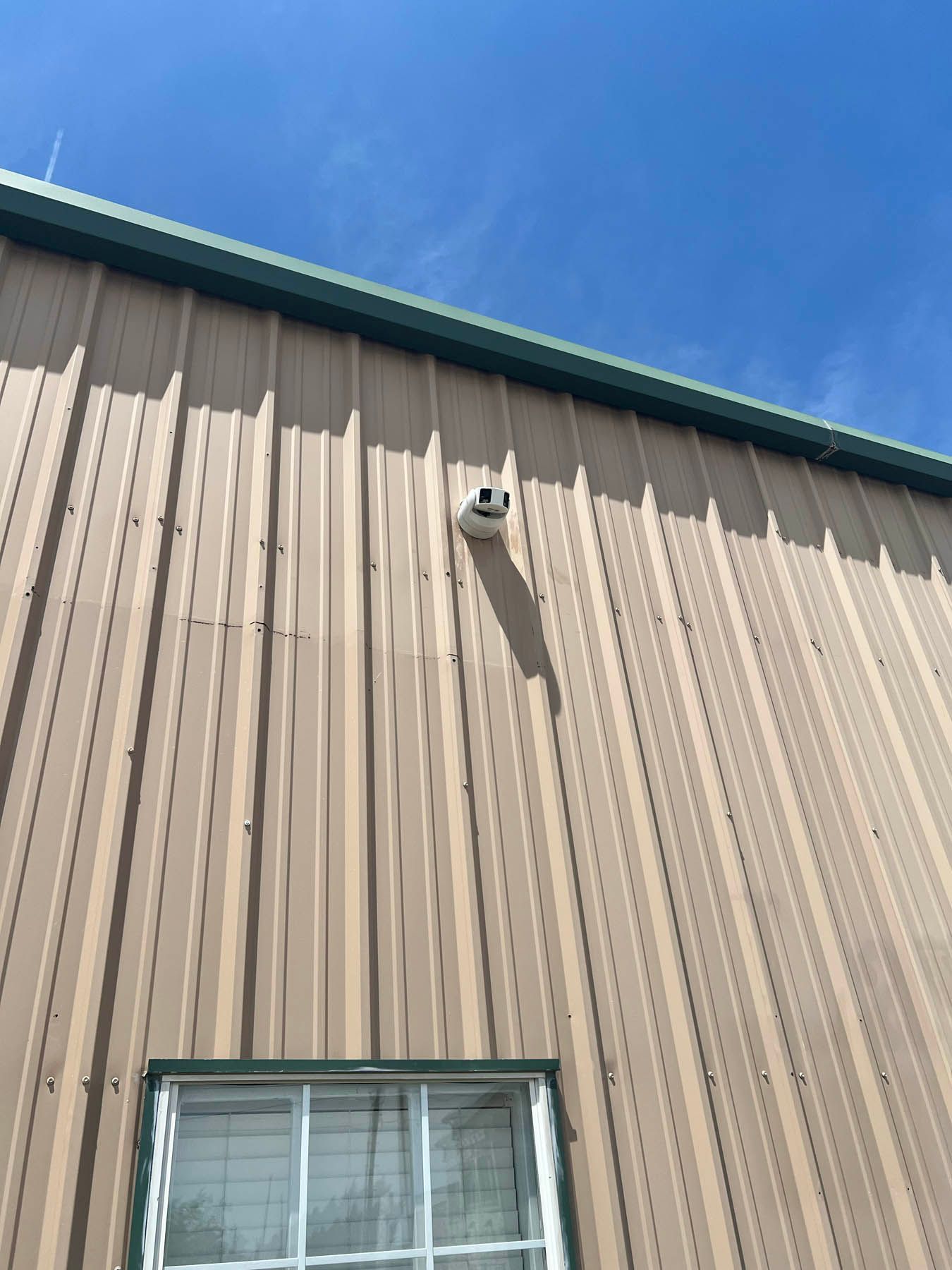 Tan metal building wall with security camera and window against a blue sky.