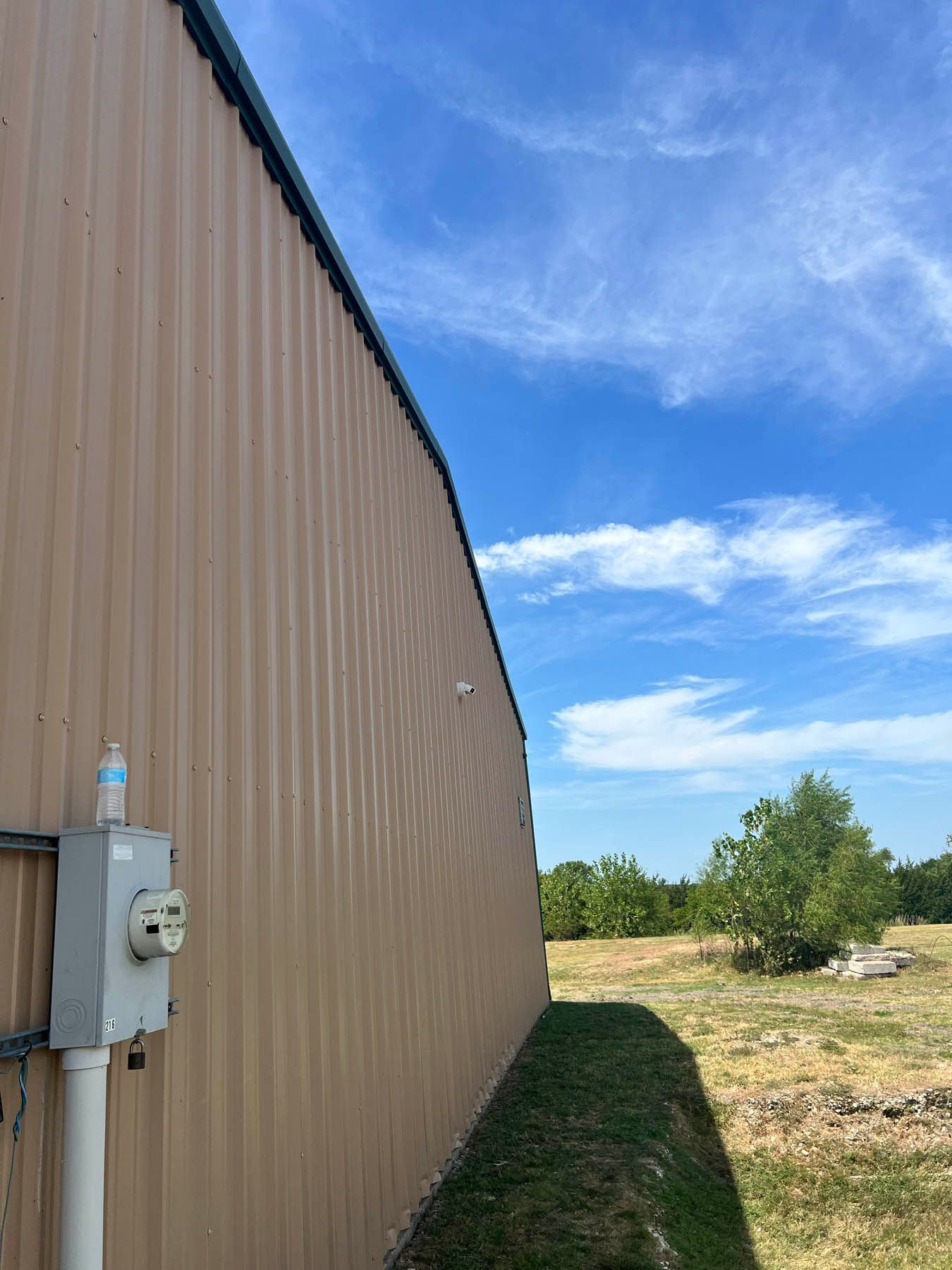 Tan industrial building exterior with electrical box against a bright blue sky.