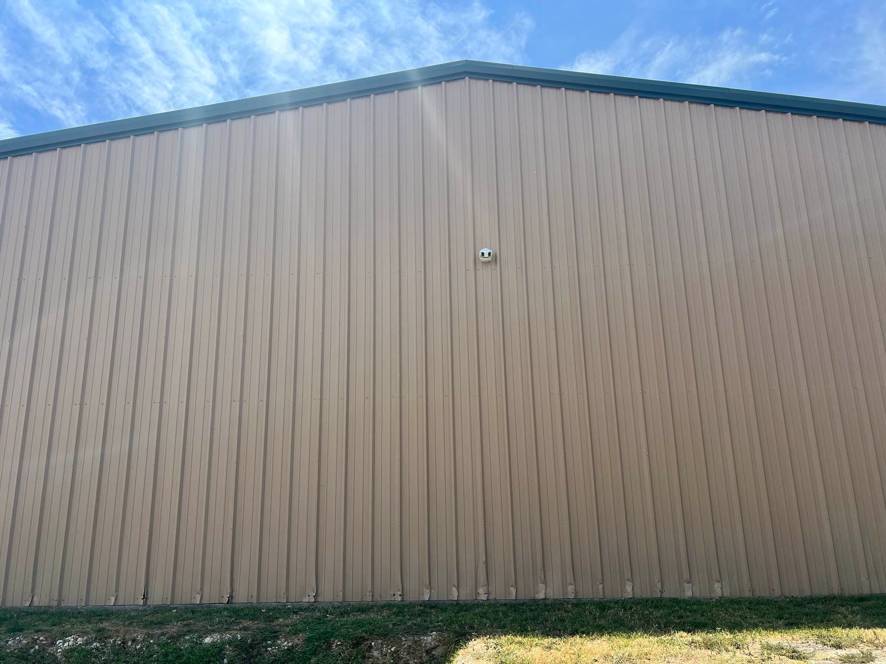 Tan metal building with green trim against a partly cloudy blue sky.
