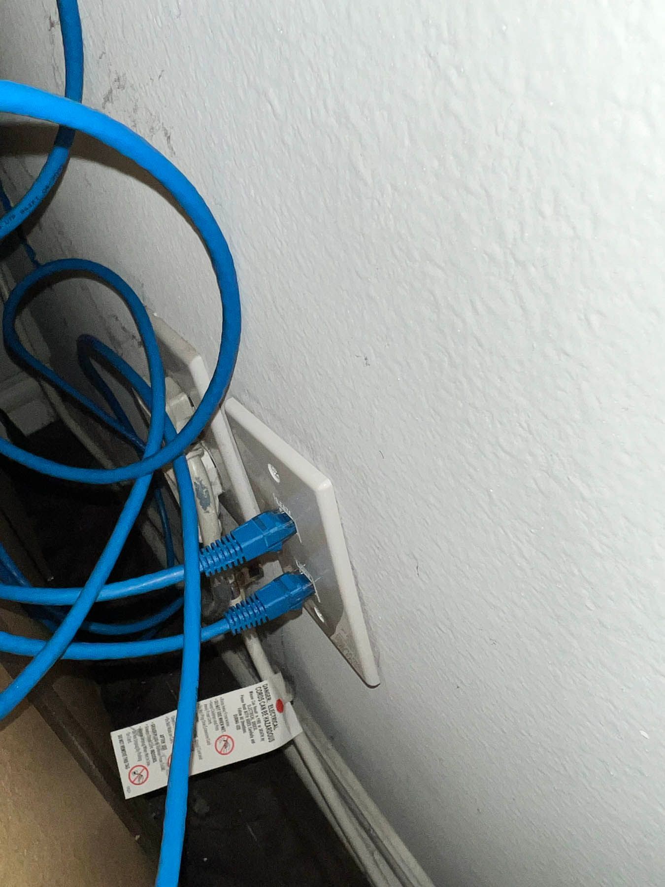 Blue Ethernet cables plugged into a white wall outlet. A portion of a dark surface is visible.