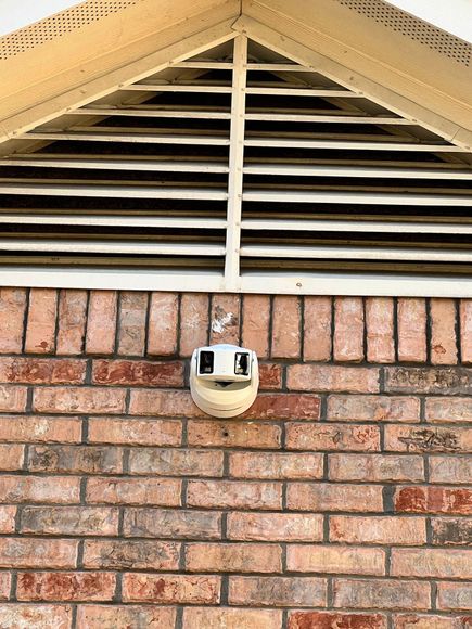 Brick building exterior with a security camera below a triangular vent.