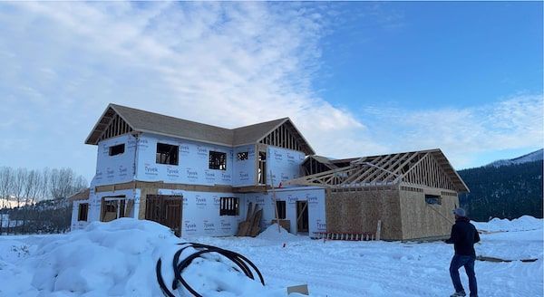 House under construction in a snowy field, wood frame visible, blue sky overhead.