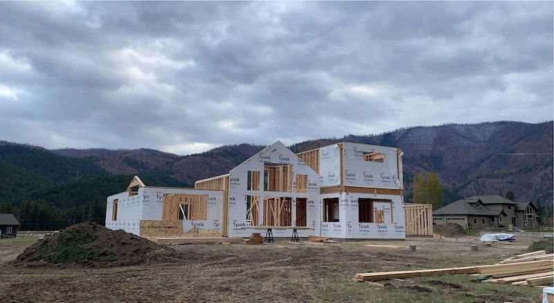 Construction of a two-story house with wooden framing and sheathing, set against a mountain backdrop.