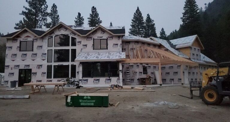 House under construction, exterior covered with wrap, surrounded by construction materials.