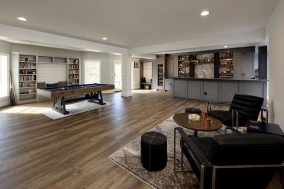 A finished basement with a pool table, bar, and seating area. Light wood floors, white walls, and gray accents.