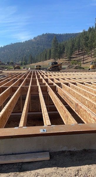 Wooden floor joists being constructed on a concrete foundation, with a mountain backdrop.