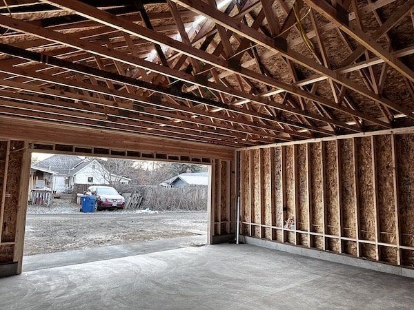 Framed interior of a garage under construction with exposed wood beams and an open doorway.