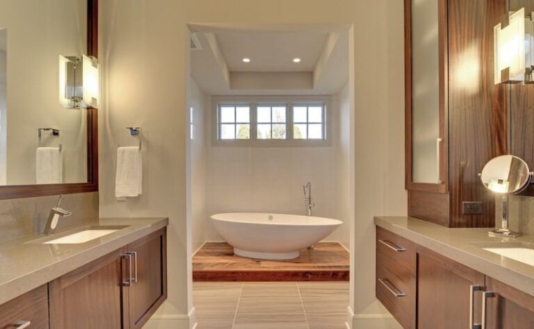Modern bathroom with double sinks, wooden cabinets, and a raised bathtub under a window.