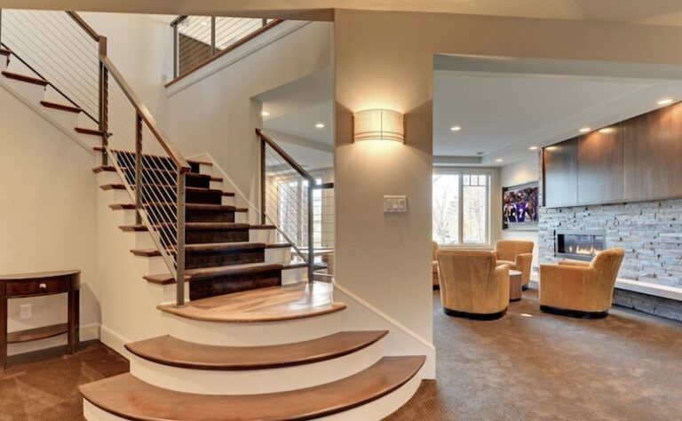 Staircase with wooden steps and metal railing leads to a second level. An adjacent living room with chairs is visible.
