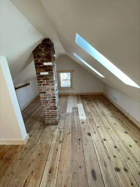 Attic room with wood floor, exposed brick chimney, and natural light from skylights.