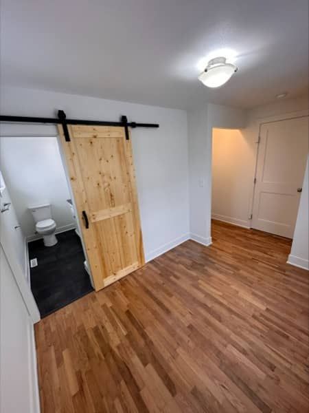 Room with wood floor, a bathroom with sliding barn door, and another doorway.