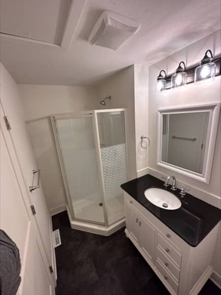 Bathroom with white walls, dark floor, vanity with black top, and a glass shower.