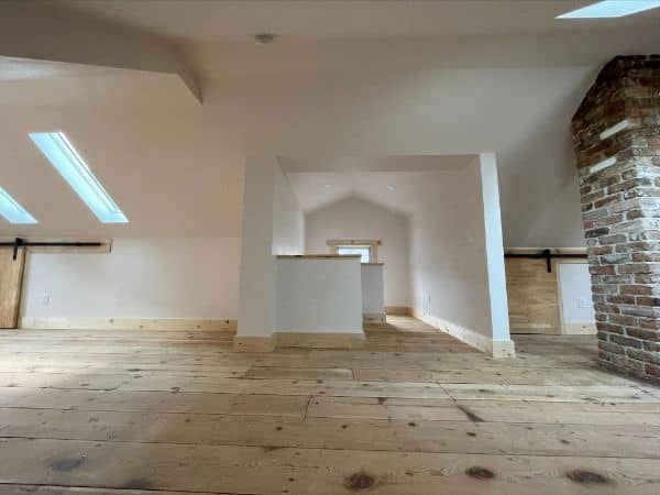 Spacious attic interior with wooden floors, white walls, and exposed brick chimney.