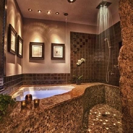 Luxurious bathroom with a jacuzzi, mosaic tiles, and rainfall shower. Warm lighting and a stone wall add to the ambiance.