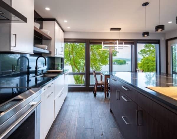 Modern kitchen with dark countertops, white cabinets, and a large window overlooking a lake.