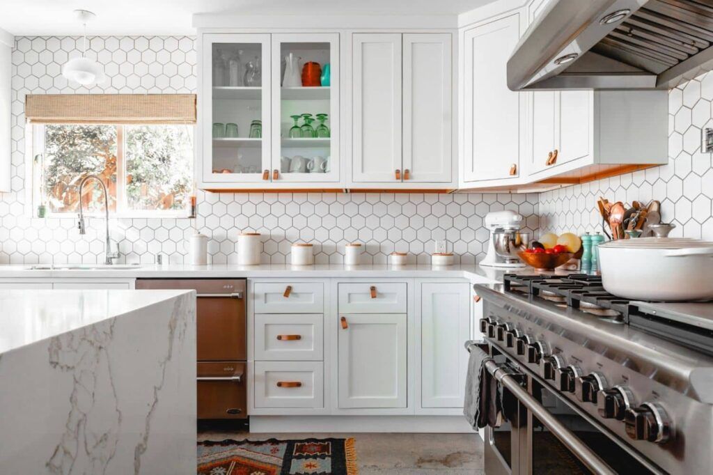 Bright white kitchen with hexagon tile backsplash, white cabinets, copper hardware, and stainless steel appliances.